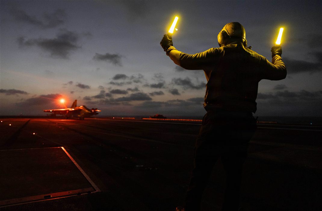 Navy carrier flight deck handler signaling aircraft with glow wands during night operations